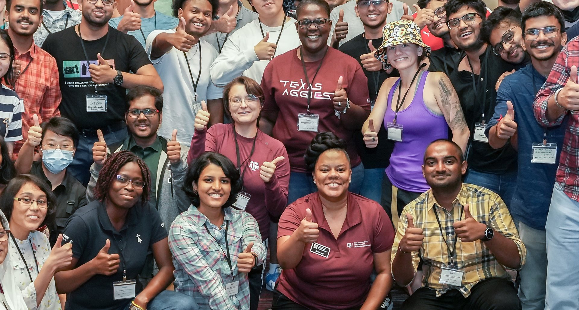 A large group of students and staff flashing a "gig 'em" thumbs-up sign 
